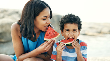 A mother and son eating slices of watermelon together.