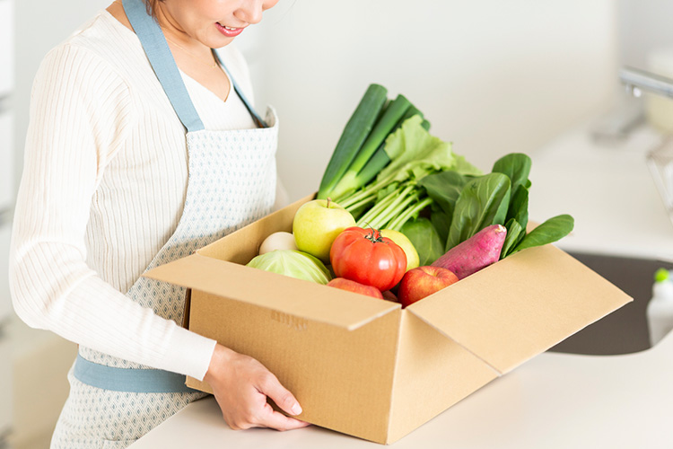 Woman with a full box of produce in hand.